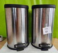 Front view showing two cylindrical chrome garbage cans with black bases and pedals.