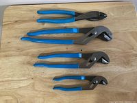 Four blue-handled pliers arranged on wooden surface including two larger tongue & groove, one medium V-jaw, one small tongue & groove