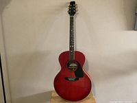 Front view of the red Aspen acoustic guitar missing one string, showing black pickguard and six tuning pegs