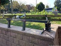 Full side view of the EZ Green crossbow press on a stone ledge outdoors showing its metal frame and legs.