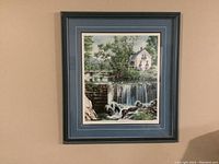 Full view of the framed print illustrating a waterfall with trees and a white house, double matted in blue and black frame.