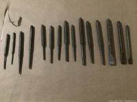 Full view of 15 pieces of metal punches and chisels laid out on a brown surface in varying lengths and tip shapes.