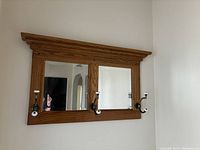 Front view of the oak framed mirror with two square mirrors and four brass and porcelain hooks on the bottom of the frame.