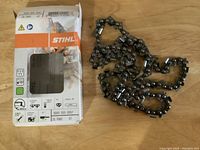 Photo shows a new STIHL 16-inch chainsaw chain beside its original branded packaging box, both placed on a wooden surface.