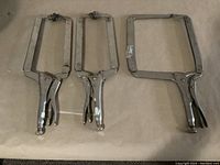 Photo showing three locking C-clamps side by side on a flat surface. Clamps are metal with lever lock mechanisms and adjustable screws. The largest is branded Irwin Vise-Grip, the two smaller clamps are unbranded.