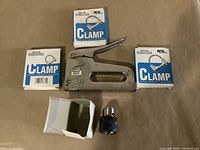 Photo showing the heavy duty stapler, three unopened boxes of Roll heavy duty medium crown staples, and a black and silver drill chuck with its box on a beige surface.