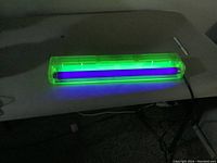 Blacklight fixture powered on showing purple glow from bulb inside translucent green housing.