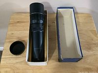 Photo showing Zeniton lens in original box with lens cap off to the side lying on a wooden table