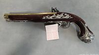 Toy flintlock pistol replica with decorative silver detailing and wooden body visible from the side.