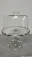 Full view of transparent glass cake stand with dome cover on a flat surface.