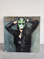 Single album cover of The Joe Walsh Band 'The Joker' showing a man in a black leather jacket and green mask with hands behind head.