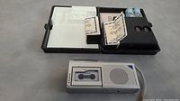 Two items: silver Sanyo microcassette tape recorder with visible cassette inside and black medical test kit with reagent compartments and vials