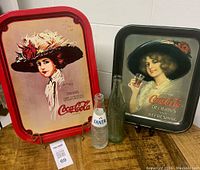 Overview of two Coca-Cola tin trays and three empty vintage glass bottles including a Fanta bottle