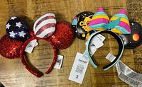Photo showing both Disney ears headbands; one with American flag red sequined ears, the other with Lightyear space themed ears and colorful bow.