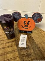 Front view showing Mickey pumpkin light-up decoration with orange pumpkin face, spider web ears, 'Trick or Treat' text, and black Tervis Hocus Pocus tumbler with purple lid.
