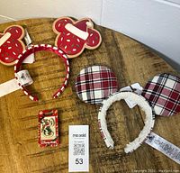 Both holiday ears headbands and the Christmas pin displayed on wooden tabletop, showing their new tags and condition.