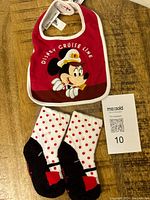 Disney Cruise Line baby bib with Minnie Mouse and polka dot socks, displayed flat on wood table