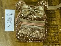 Front view of rose gold sequin Minnie Mouse Loungefly wristlet with ears and gold bow, resting on wooden surface