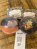 Two unopened Disney holiday ornament pins, one featuring Dumbo the elephant and the other a Nativity scene, each in a plastic protective sphere with backing card labelled "Disney Pin Ornament."