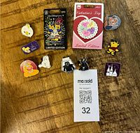 Top view of 11 assorted Disney pins laid out on a wooden surface, including two new pins on cardbacks: a 2021 Happy New Year pin and a Valentine's Day heart pin. The other 9 are trading pins featuring various characters including Donald Duck, Lady, Snoopy, Rocket Raccoon, Winnie the Pooh, and a castle icon.