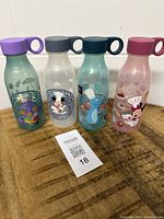 Front view of four Disney plastic bottles with characters Figment, Mickey, Remy, Minnie showing colorful illustrations and loop caps.