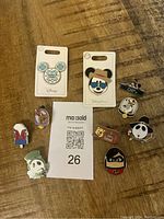 Full set of 8 Disney trading pins displayed on wooden surface with auction lot paper