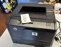 Front angled view of black HP LaserJet Pro 400 M401n printer showing top paper output slot, control panel, and HP logo.
