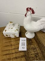 Photo of white milk glass rooster figurine and square covered dish with gold accents on wooden surface.