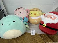 Four Squishmallows including crab, cup, chick, and Santa plush