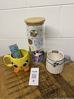 Photo of the full set showing two Disney-themed mugs and the clear canister with bamboo lid arranged on a wooden surface