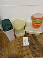 Tupperware set displayed on wooden surface against white wall, showing various containers and some lids.