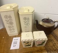 Full view of flour and sugar containers, salt and pepper shakers, and ceramic teapot on wooden surface