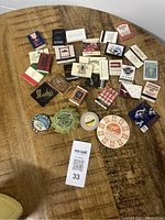 Lot of vintage matchbooks and four old milk bottle caps on wooden surface with MaxSold label, showing a variety of matchbook designs from different establishments including restaurants and motels.
