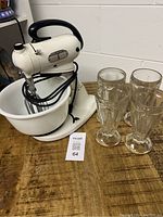 Vintage Hamilton Beach mixer with white bowl and 4 vintage milkshake glasses on a wooden surface.