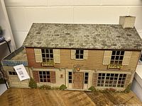 Front exterior view showing two-story metal lithograph dollhouse with window shutters, flower boxes, and front door.