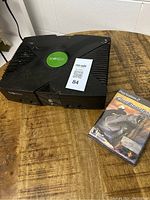 Black original Xbox console with green logo and unopened PS2 Cool Boarders game on wooden table