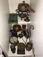 Inclined view showing the fondue pot on stand, set of six fondue forks in case, metal bell, and assorted candle holders and metal items.
