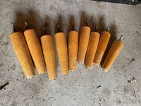 Nine tapered wooden chair legs with integrated screws and floor glides laid on concrete floor showing wear and finish flaws.