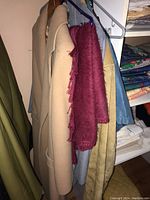 Clothing on hangers in closet showing suede jacket, colorful scarf, various wool and cotton garments.