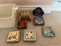 Full view of assorted coasters and holders arranged on carpet, showing variety of styles and materials