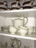 Photo of the coffee pot, cups and saucers arranged on shelf showing white porcelain with brown decorative banding and gold trim.