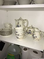 Shelf view of the entire Zsolnay coffee set showing coffee pot, sugar bowl, creamer, six cups and six saucers with detailed floral patterns.