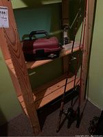 Photo of fishing rods, tackle box, and lantern on wooden shelf in basement corner