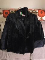 Front view of short black fur coat on hanger showing overall style, collar, and button closure.