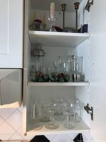 Shelves in a cabinet with various glasses, candle holders and a martini mixer