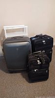 Three suitcases including one large Heys hard-sided and two smaller American Tourister soft-sided luggage pieces placed on carpeted floor