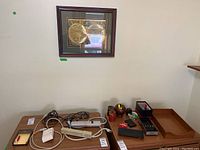 Wide shot showing framed vintage map on wall above wooden surface with assorted office supplies including power bars, cables, pens, trays, and holders.