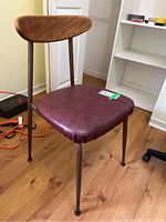 Photo of Mid Century Modern chair showing a burgundy cushioned seat, wooden curved backrest, and metal tubular legs on a wood floor.