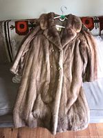 Front view of light brown mink fur coat hung on a hanger, showing overall shape and length with buttons fastened.