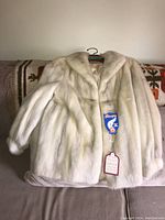 Full view of the light mink fur jacket displayed on a hanger showing front, soft cream color with a few subtle darker tones.